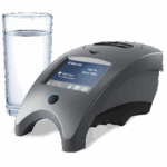 A modern WaterLink Spin Touch DW Sales Demonstration Outfit - 4-3085 digital water testing device with a touchscreen display sits next to a clear glass filled with water on a white surface.