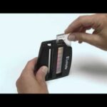 A person inserts a test strip into a black BrewLab Pro - 7190 handheld water testing device with a color chart visible on its side.